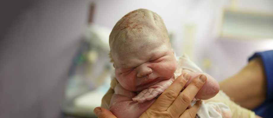 Cloe-up on newborn baby held by midwife